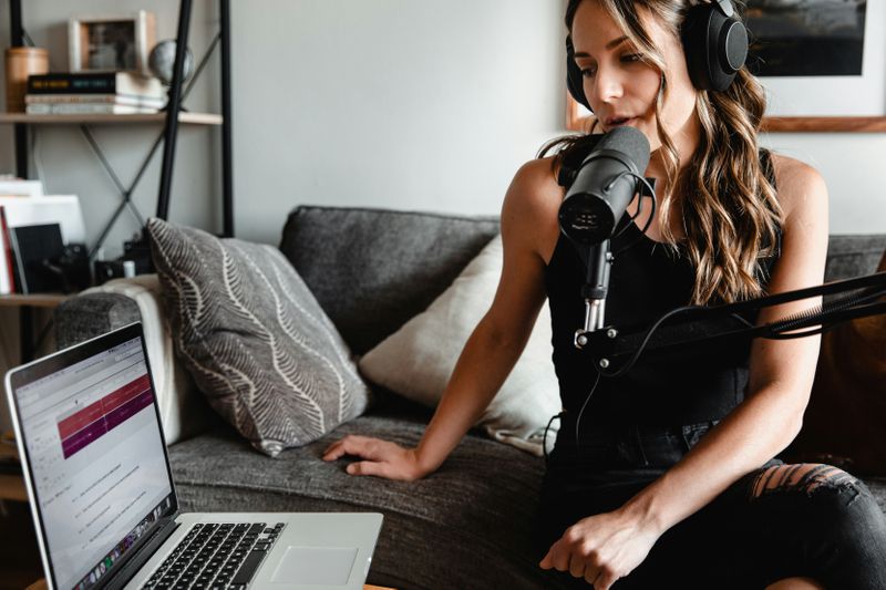 A woman speaking into a mic while on laptop.