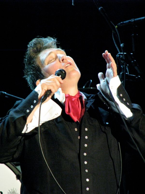 music artist k d lang singing into a microphone dressed in an androgynous jacket and ascot