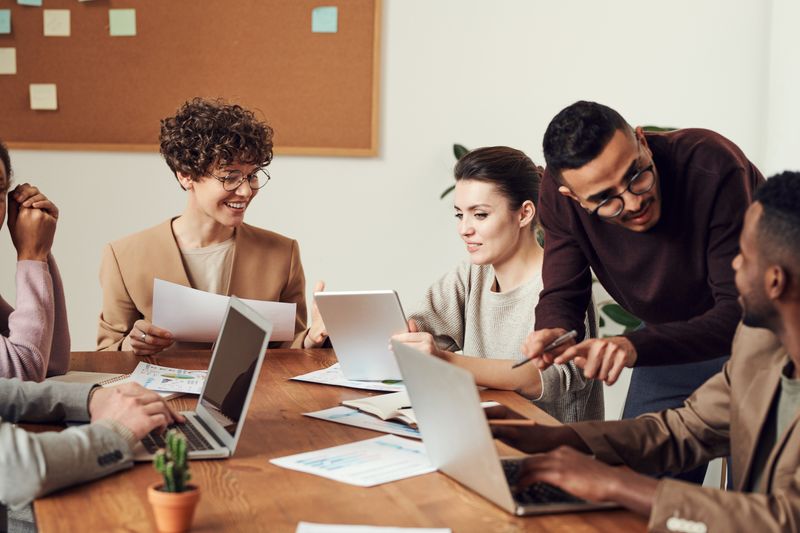 Group of people sitting inside at table with laptops (Photo by fauxels from Pexels)