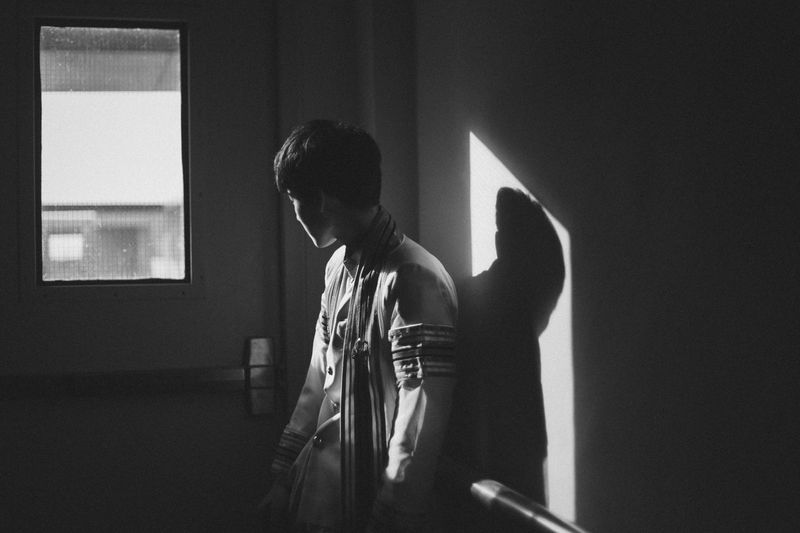 A teenage boy alone in a room looking out the window.