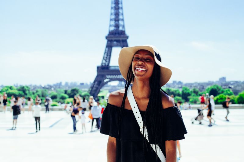 A joyful woman poses smiling in front of the Eiffel Tower