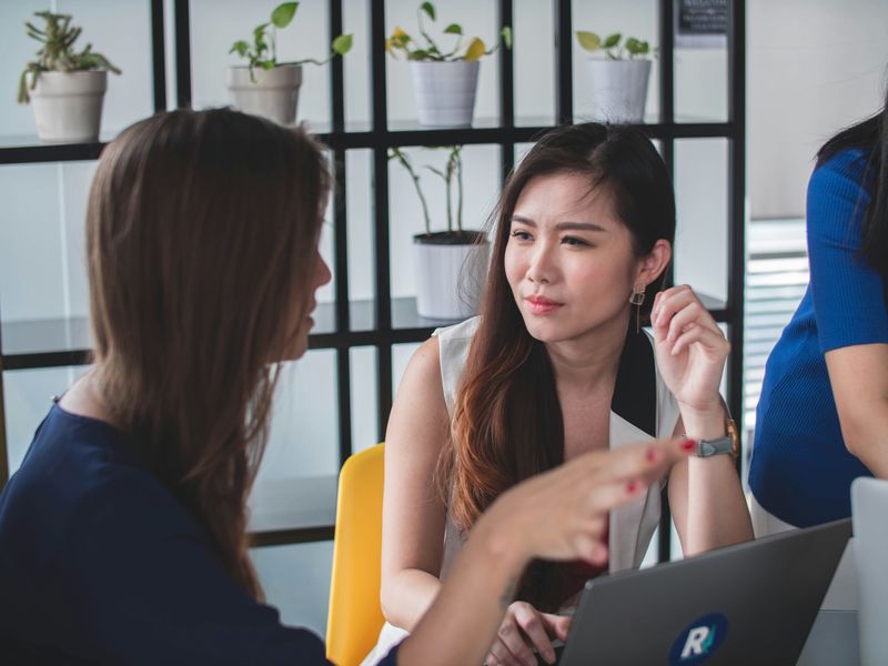 A photo of a lady talking to an Asian colleague in an office.