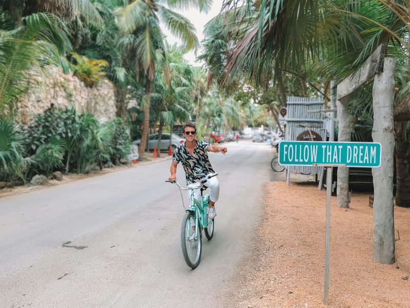 A person on a bike in an exotic location. He points to a sign that reads: 