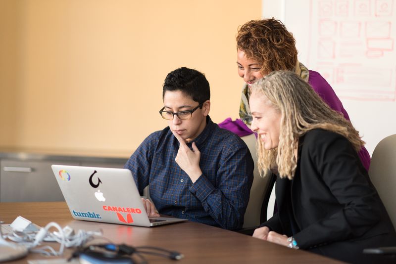 Three people of different races are sitting around a table and laptop.