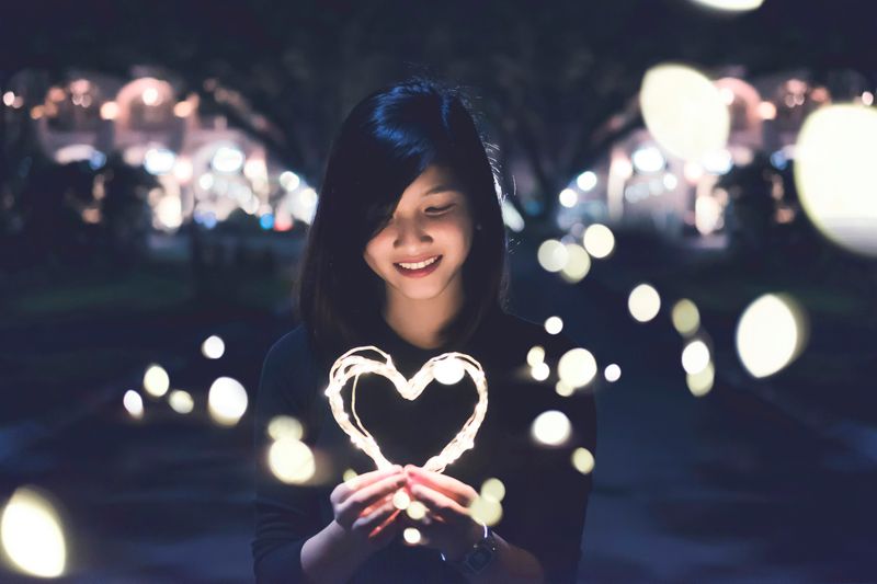 A young person holding heart-shaped lights, smiling to symbolize self-love and calm.