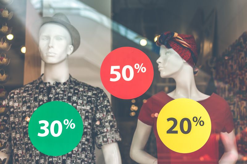 Mannequins in a store window display with discount circles around them reading 30%, 50%, and 20%.