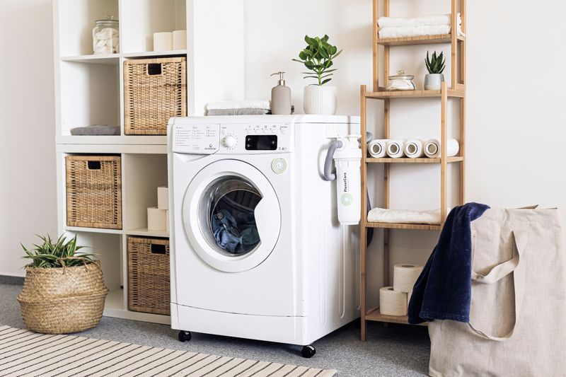 A laundry room with a white machine and shelves along with brown wicker baskets and a plant.
