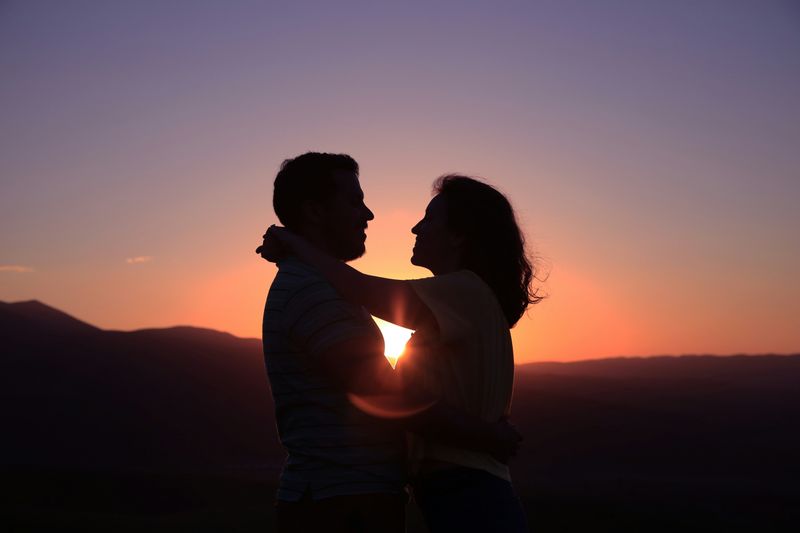 Image: Silhouettes of a couple embracing tenderly under a colorful sunset.