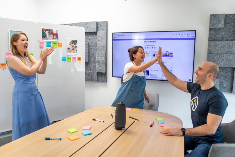 Three colleagues celebrating at work. Two give a high-five. One claps hands.