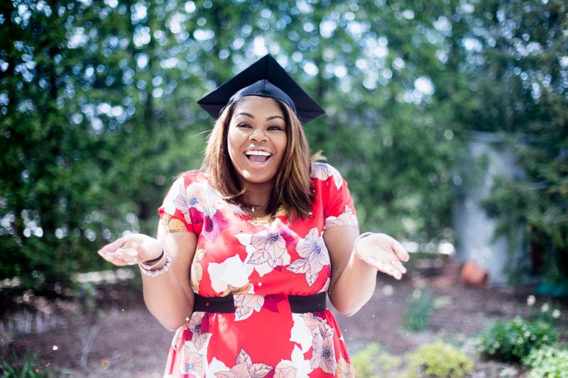 A Black college student wearing a graduation cap, shrugging her shoulders.