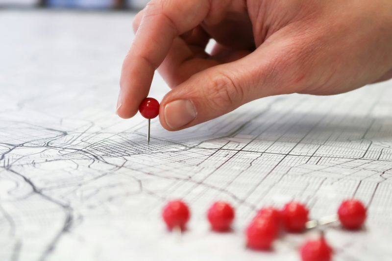 A hand putting red pushpins into points on a white map with black lines.