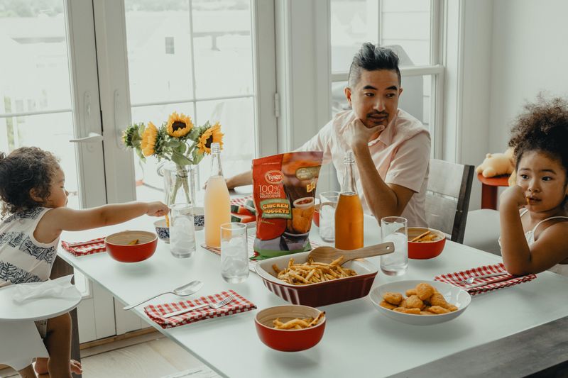 Dad eating chicken nuggets at the kitchen table with two children.