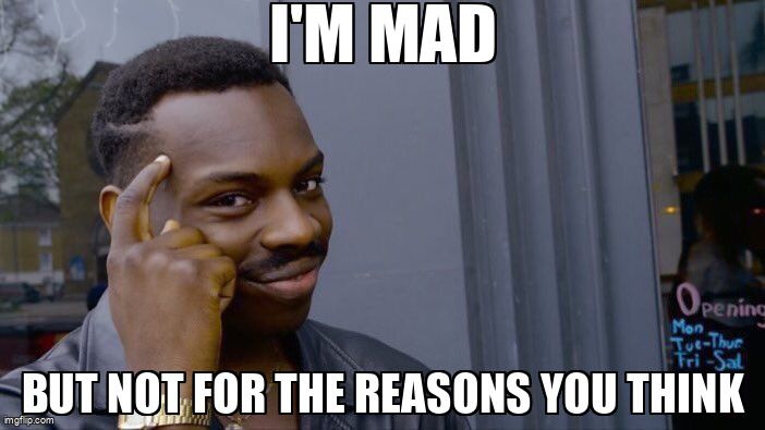 A man pointing to his forehead with a smirk on his face. He says, 'I'm mad, but not for the reasons you think.'