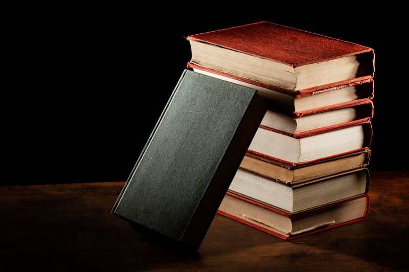 A picture of a black book leaning on a stack of books.