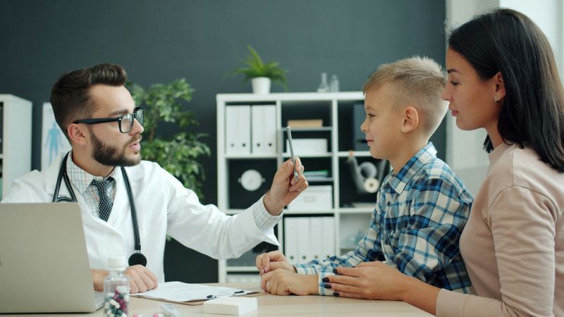 A doctor demonstrating emotional intelligence in appointment with mother and child.
