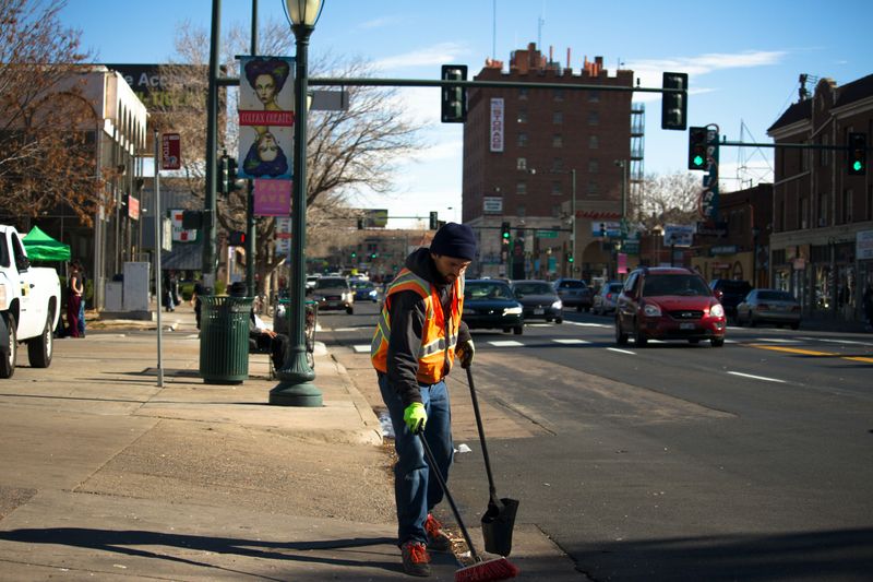 A sanitation worker sweeping trash from the sidewalk with a broom.