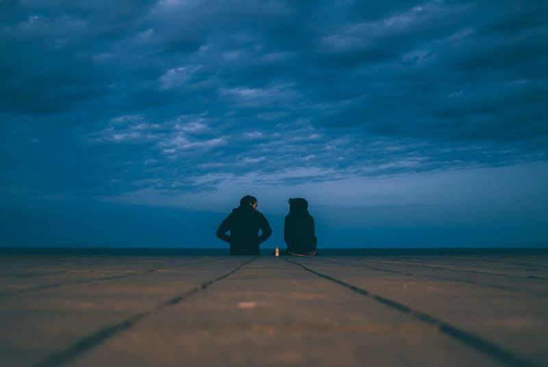 An image of two people sitting on concrete next to each other looking at one another.