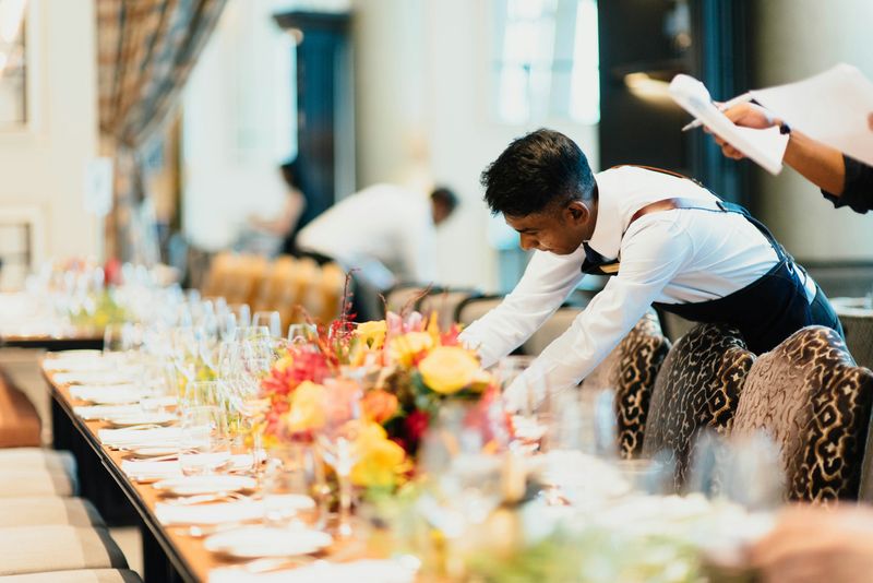 A person setting a long table in a restaurant.