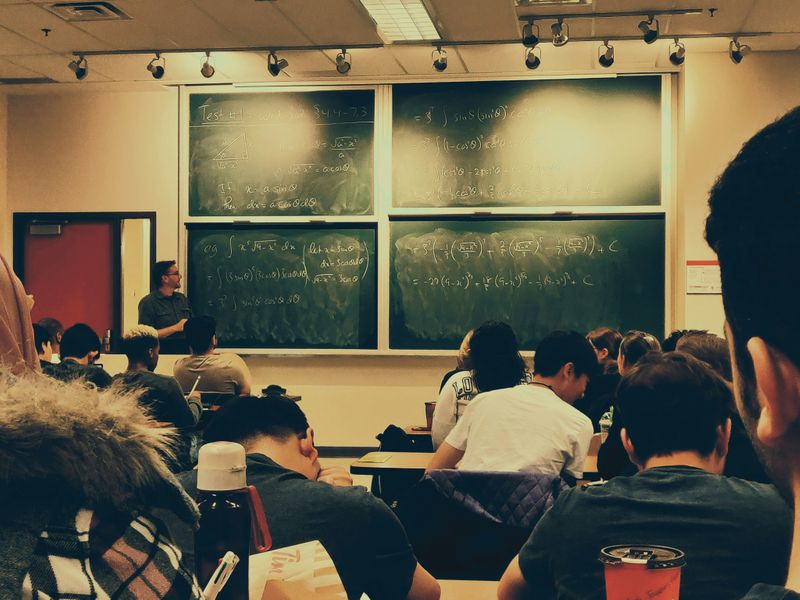 A classroom filled with students and math problems on a chalkboard.