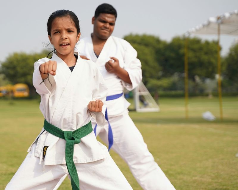 A girl and boy in karate uniforms wearing green and blue belts.
