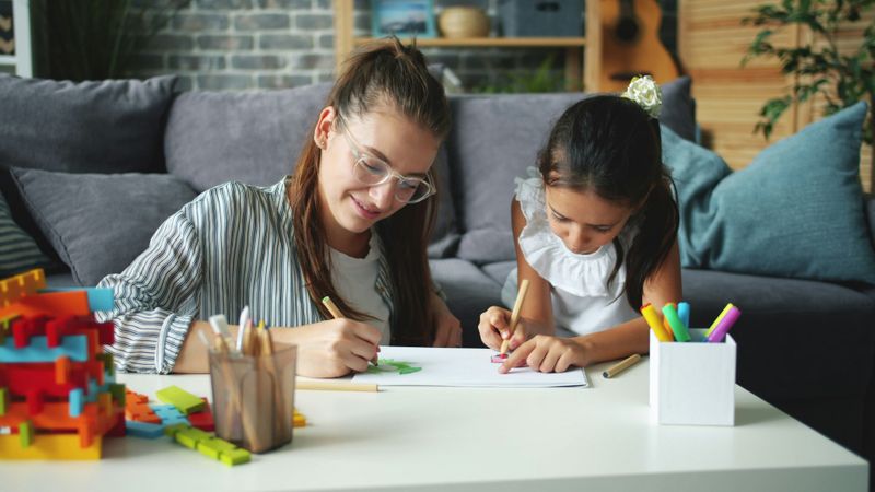 A young woman and little girl coloring at a table together.