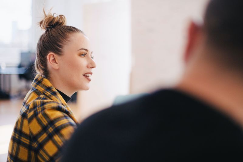 Image of a young woman sitting at a table in conversation, captivating the listeners.