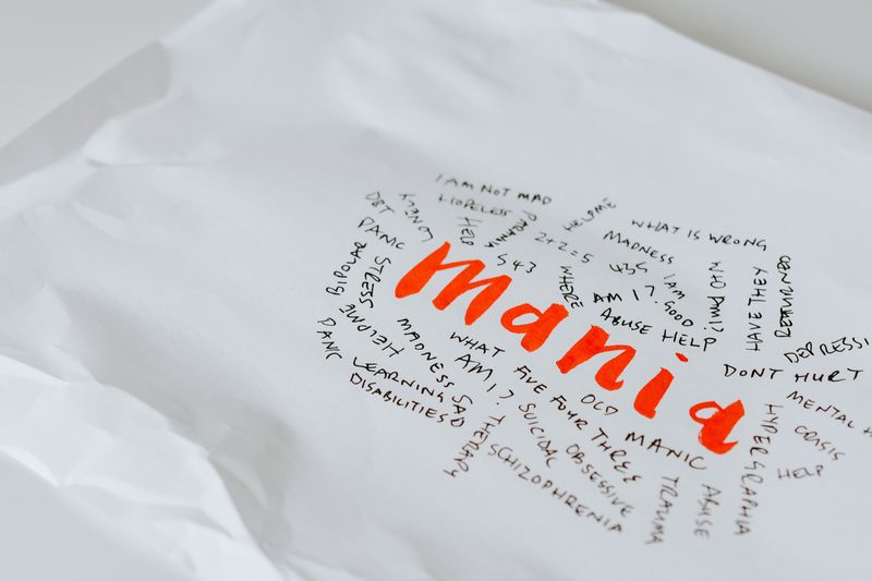 Paper with the word :mania' and other text around it expressing how a person may feel.