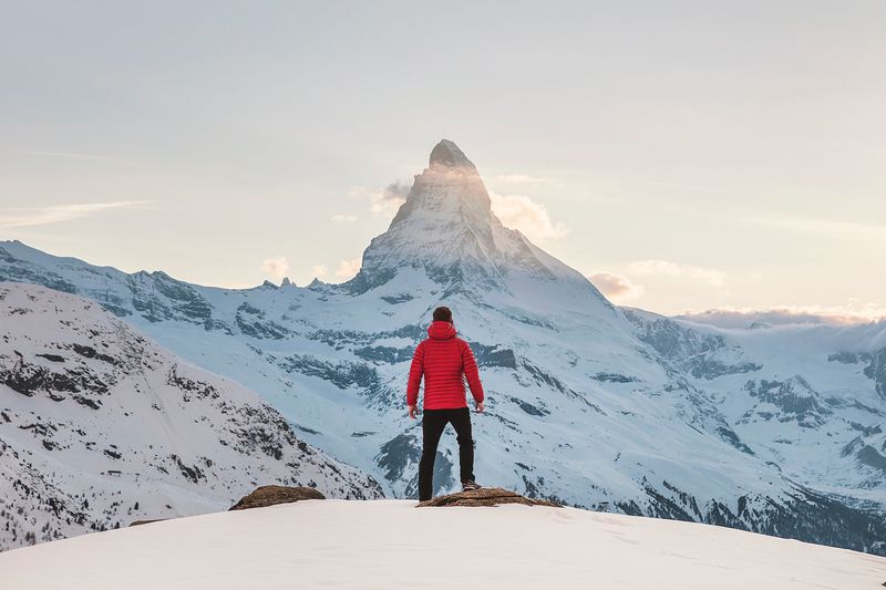 A man stands on a snowy mountain and is staring at the peak which isn't far away
