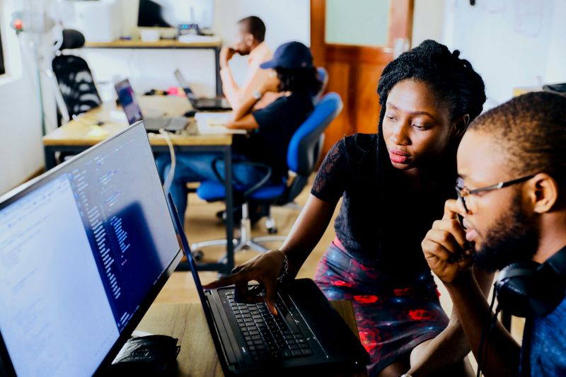 Two people using AI for coding, discussing some work on a computer in front of them. 