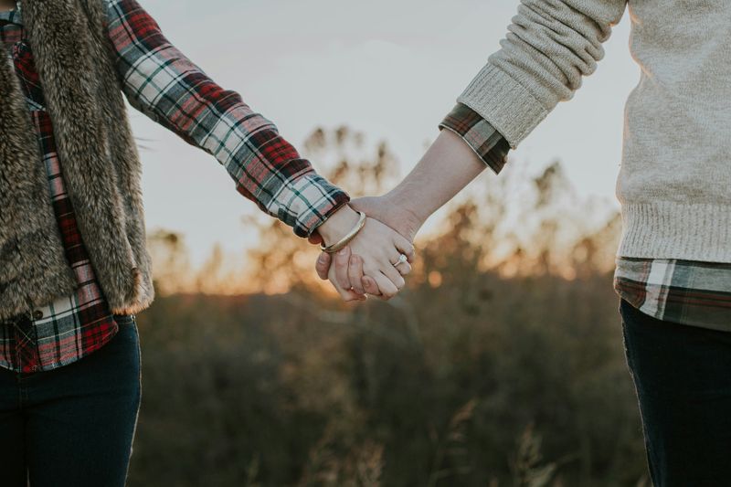 A couple holding hands in a meadow at sunset.