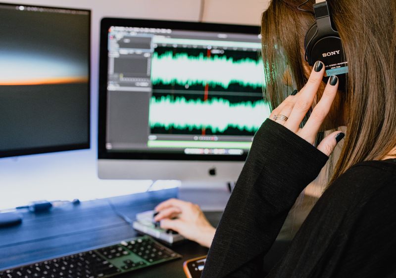 Partial image of a female wearing headphones sitting at a desk adjusting sound volume buttons on a keyboard