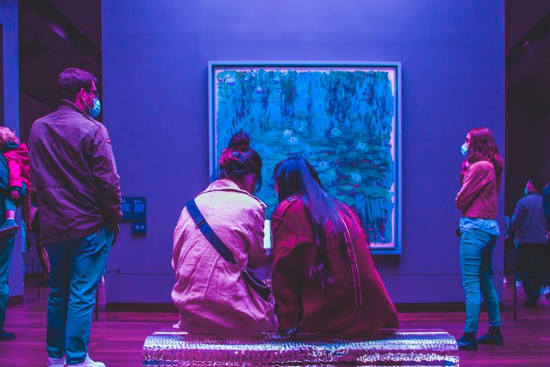 Two women sitting on a bench in front of a Monet waterlily painting.