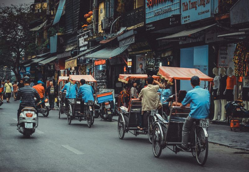 People drive rickshaws and mopeds along a busy street in Vietnam.