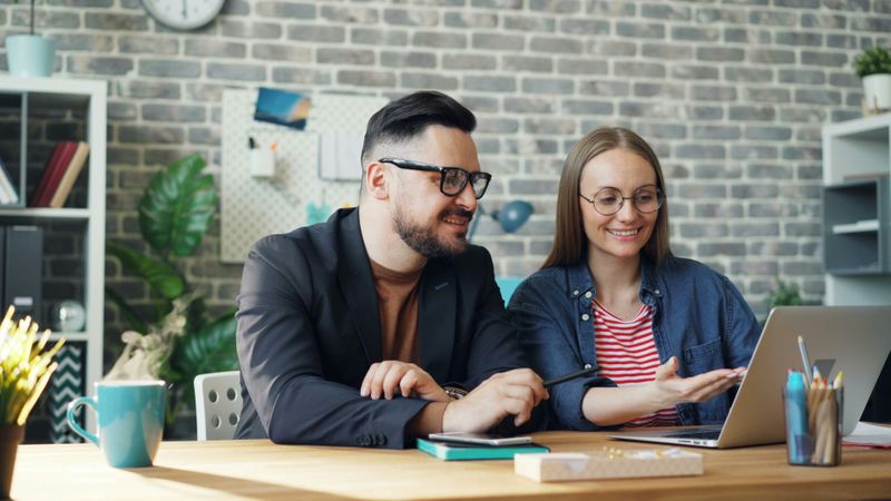 A man and a woman talking while looking at a laptop.