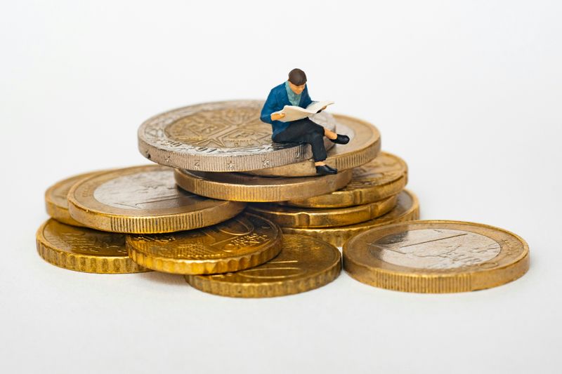 A figure of a man sitting on gold coins, reading a newspaper.