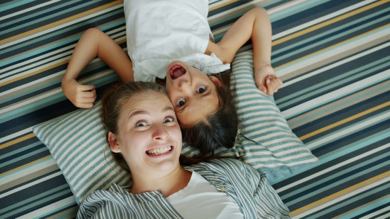 A young women and a little girl lying down making silly faces.