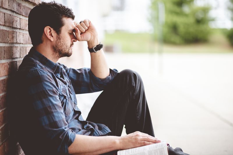 A disappointed young adult sitting by a wall.