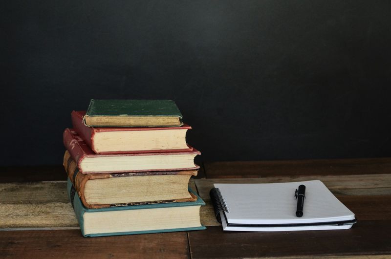 A stack of books with a notebook and pen on a table. 