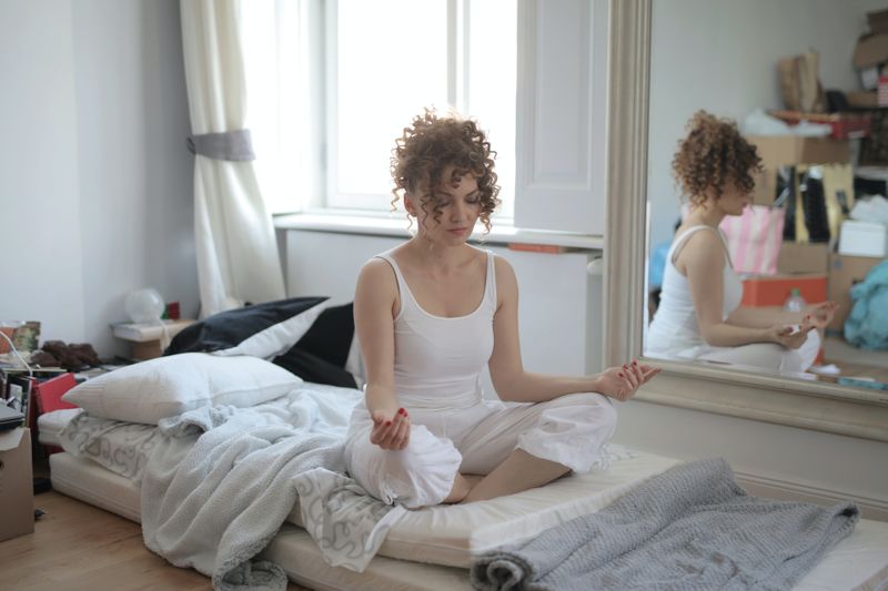 women meditating on a messy bed surrounded by boxes