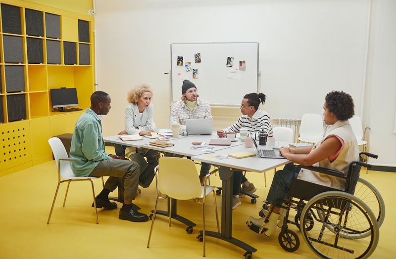 A group of people with variety of gender, racial background, and physical abilities in a work meeting together.