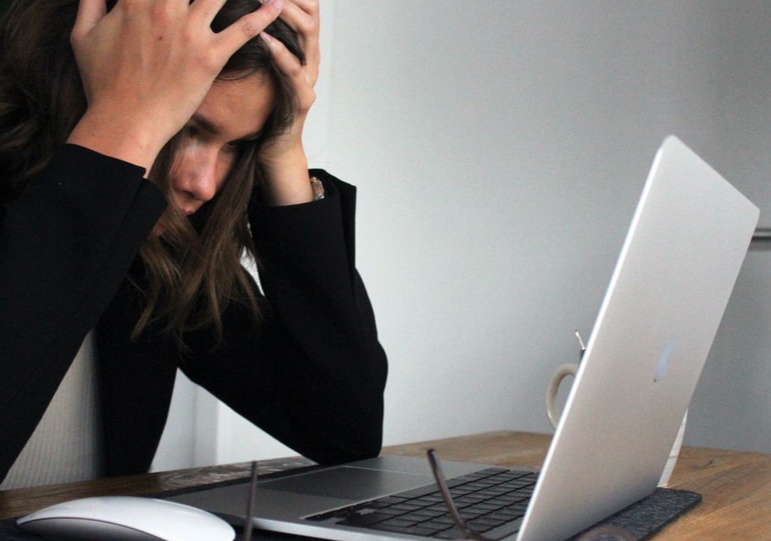 Stressed woman with head in her hands looking at the computer screen.