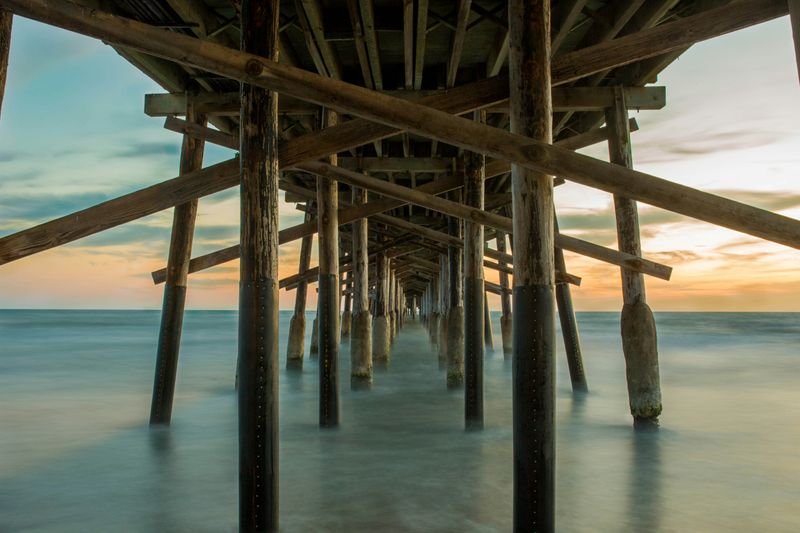 An point of view from beneath an ocean pier, with many support struts holding the pier up.