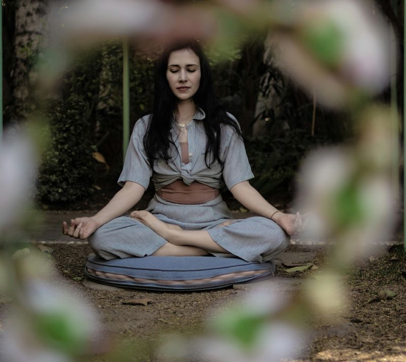 A women is sitting with her leg crisscrossed, eyes closed, and her arms are down with her palms up. She looks relaxed.