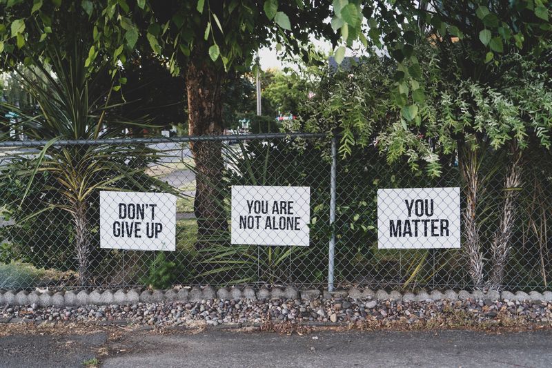 A gate in front of exotic vegetation with posters saying 'Don't give up', 'You are not alone', 'You matter'.