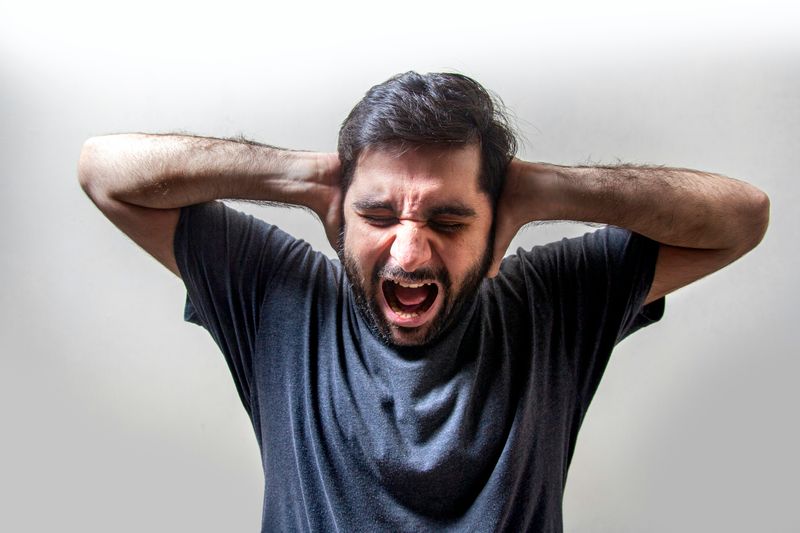 A frustrated man screaming with his hands over his ears, showing signs of stress.