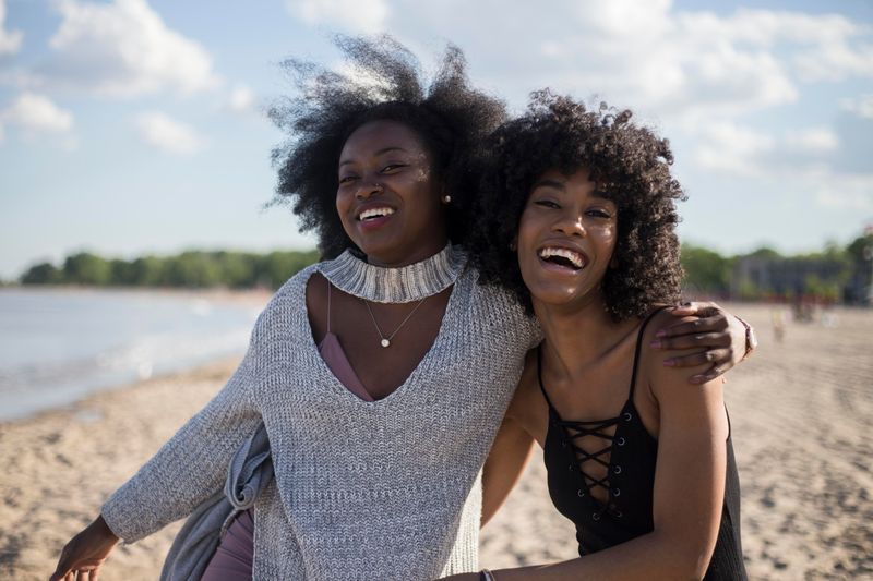 Two smiling friends side by side on the beach.