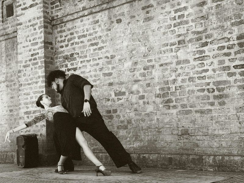 Two people dancing tango in front of a brick wall.