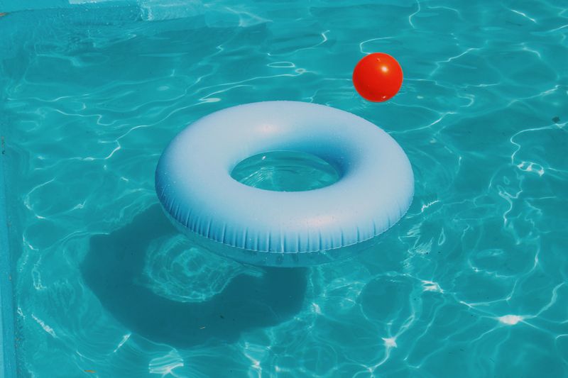 A blue floatie and a red ball floating in pool water.