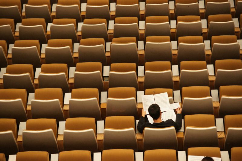 A man studies alone in a room with rows of empty yellow chairs. 