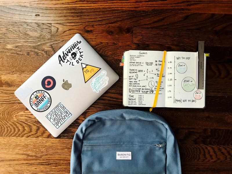 A laptop, a blue backpack, and an open planner on a desk.